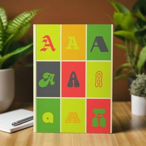Könnte beinhalten: Ein Notizbuch mit einem bunten Umschlag, der verschiedene Stile des Buchstabens "A" in einem Rastermuster zeigt. Der Umschlag ist gelb, orange, grün, rot und grau.