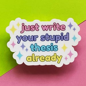 May include: A white sticker with the text "just write your stupid thesis already" in pink, blue, and yellow. The sticker has a white border with colorful star accents and is set against a green and pink background.