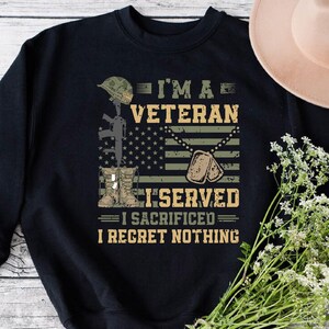以下が含まれることがあります： 兵士、アメリカ国旗、ドッグタグ、そして「I'm a Veteran I Served I Sacrificed I Regret Nothing」というテキストがプリントされた黒いスウェットシャツ。