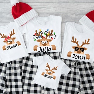 May include: Four white t-shirts with a reindeer design and personalized names: Olivia, Julia, John, and Noah. The shirts are paired with black and white plaid pants.