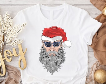 May include: White t-shirt featuring a graphic of a bearded man wearing a Santa hat and sunglasses. The illustration has a detailed design with a red hat, gray beard, and black sunglasses. The shirt is a classic crew neck.