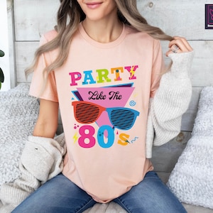 May include: A pink t-shirt with a graphic design featuring the text "Party Like The 80's" in colourful letters and a pair of sunglasses with a retro design.