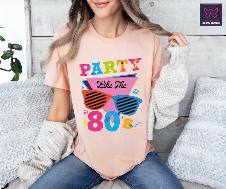 May include: A pink t-shirt with a graphic design featuring the text "Party Like The 80's" in colourful letters and a pair of sunglasses with a retro design.