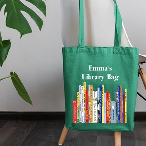 May include: Green canvas tote bag with the text "Emma's Library Bag" and a colorful illustration of a stack of books.