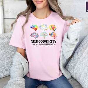 K&ouml;nnte beinhalten: Pinkes T-Shirt mit einer Grafik von bunten Hirn-Umrei&szlig;ungen und dem Text "Neurodiversity We All Think Differently".