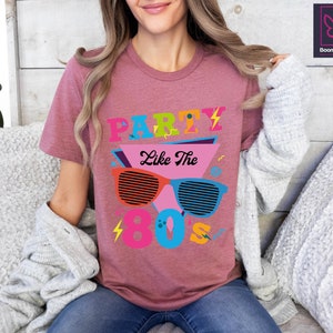 May include: A pink t-shirt with the text "Party Like The 80's" in colourful, retro-style lettering and a graphic of sunglasses with a lightning bolt design.