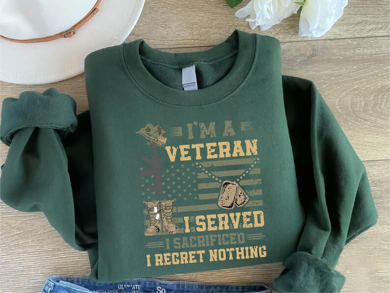 以下が含まれることがあります： 暗い緑色のスウェットシャツに、「I'm a Veteran I Served I Sacrificed I Regret Nothing」という文字が白と茶色の文字で書かれています。デザインには、軍用ヘルメット、十字架、ドッグタグ、アメリカ国旗も含まれています。