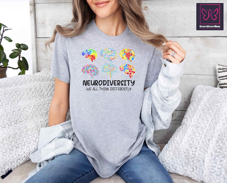 K&ouml;nnte beinhalten: Graues T-Shirt mit einem bunten Gehirndesign und dem Text "Neurodiversity We all think differently".