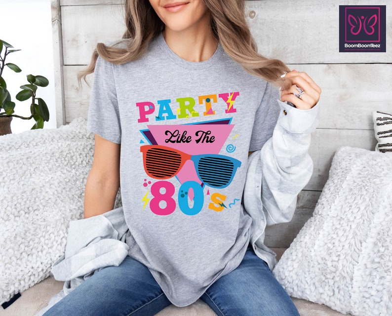 May include: A grey t-shirt with the text "Party Like The 80s" in colourful letters and a graphic of retro sunglasses.