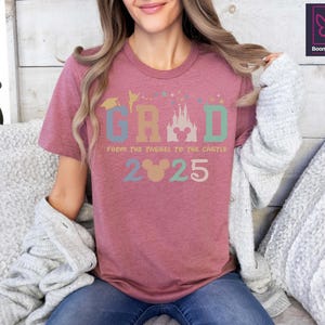 May include: A pink t-shirt with a colorful graphic that says "GRAD from the tassel to the castle 2025" with a Mickey Mouse head in the middle of the word "GRAD".