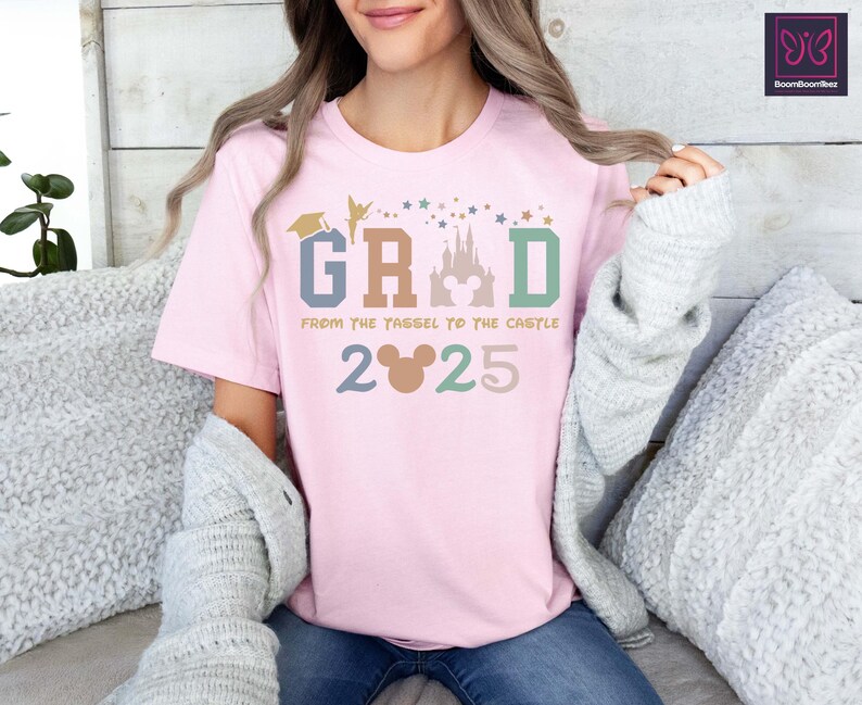 May include: Pink t-shirt with a graphic design that says "GRAD from the tassel to the castle 2025". The graphic includes a Mickey Mouse head, a graduation cap, Tinkerbell, and a silhouette of Cinderella's castle.