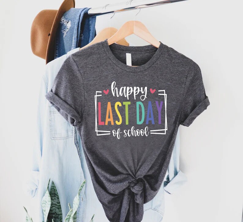 May include: A dark grey t-shirt with the text "happy last day of school" in rainbow colours and white outlines. The text is framed with a white square and two small pink hearts.