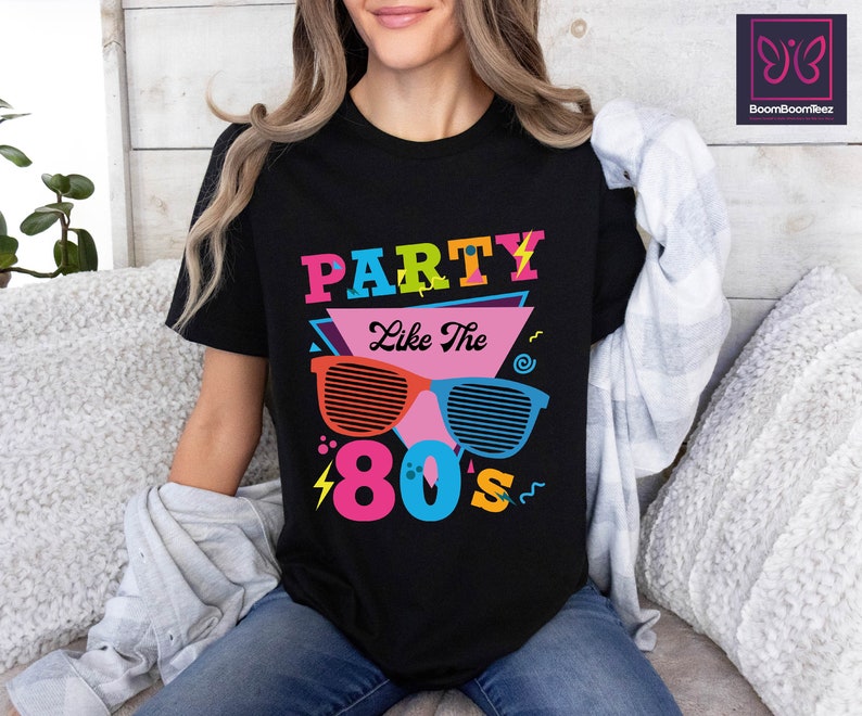 May include: Black t-shirt with a graphic design featuring the text "Party Like The 80's" in colourful letters and a pair of sunglasses with a retro design.