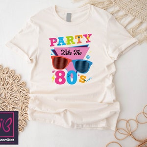 May include: A white t-shirt with a graphic design featuring the text "Party Like The 80s" in colourful letters and a pair of sunglasses with a retro design.
