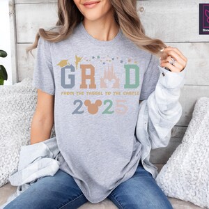 May include: Gray t-shirt with a colorful graphic of a castle, stars, and the text "GRAD from the tassel to the castle 2025" with a Mickey Mouse head.