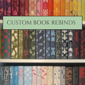 Peut inclure: Une collection de livres avec reliures personnalisées, présentés sur des étagères blanches. Les dos présentent une variété de couleurs dont le rouge, l'orange, le jaune, le vert, le bleu et le noir, avec des motifs et le texte CUSTOM BOOK REBINDS.
