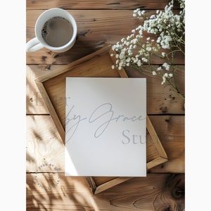 May include: A white card with the text "Baby Grace Studio" written in grey script on a wooden surface with a cup of coffee and a bouquet of white baby's breath.