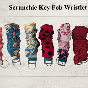 May include: Seven fabric scrunchie key fob wristlets with metal hardware and key rings. Patterns include pink polka dots, blue floral, white floral, red with black dots, pink and white floral, solid red, and purple floral. Text reads Scrunchie Key Fob Wristlet and 5" Handmade.