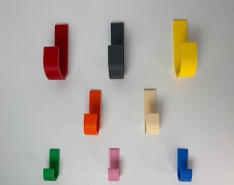 May include: A collection of nine colorful, J-shaped hooks in various shades, including red, black, yellow, orange, beige, green, pink, and blue. The hooks are arranged against a white background, showcasing their curved design.