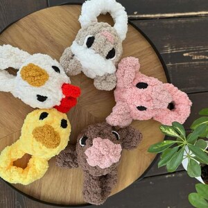 May include: Five plush animal headbands in different colours and animal designs. The headbands are made of soft, fuzzy material and feature embroidered eyes and noses. The animals include a chicken, a pig, a cow, a bunny, and a duck.