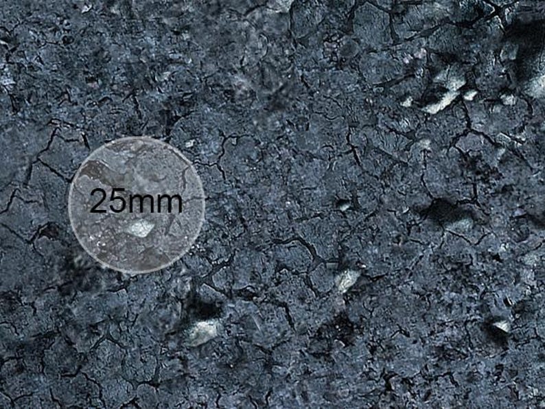 K&ouml;nnte beinhalten: Nahaufnahme einer dunkelgrauen, strukturierten Oberfl&auml;che mit einem runden wei&szlig;en Etikett, auf dem "25 mm" steht.