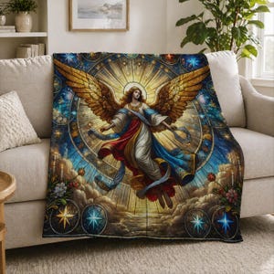 May include: A decorative throw blanket featuring a stained-glass style angel design. The angel has golden wings, flowing robes in red, white, and blue, and is surrounded by a radiant light. The blanket is draped over a beige sofa.