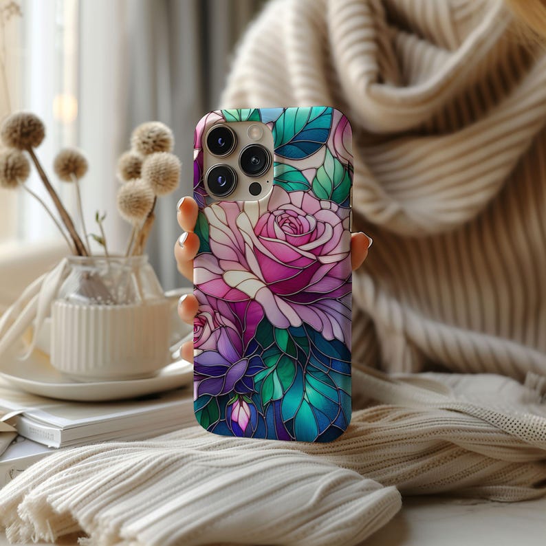 May include: A floral phone case featuring a stained-glass rose design in shades of pink, purple, and green. The case has a glossy finish and a camera cutout. The phone case is held by a person.