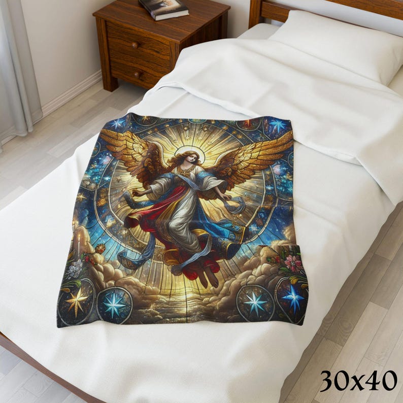 May include: A 30x40 inch blanket featuring a detailed illustration of an angel with golden wings, set against a stained-glass style background with celestial elements. The angel is depicted in flowing robes, with a halo. The blanket is placed on a white bed.