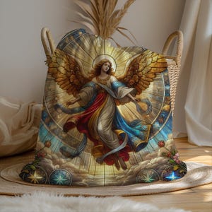 May include: A decorative storage basket with woven handles, holding a blanket featuring a stained-glass style angel design. The angel has golden wings, flowing robes, and is surrounded by a celestial background with clouds and stars. The basket sits on a woven mat.