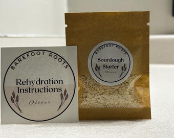 May include: A white label with black text that reads "Barefoot Roots Rehydration Instructions Oliver" and a brown paper packet with a white label that reads "Barefoot Roots Sourdough Starter Oliver".