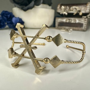 May include: Gold-toned bracelet with a geometric design. The bracelet is made of a twisted metal band with a geometric design in the center.
