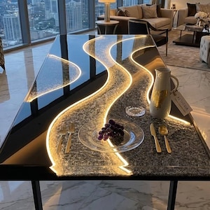 May include: A rectangular dining table with a black glossy surface and a central textured gray stone inlay illuminated by a winding LED light strip. The table features a black metal frame, a white pitcher with gold accents, and a plate of grapes.