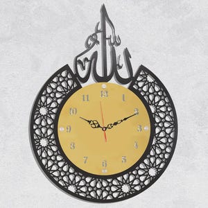 Peut inclure: Une horloge murale décorative avec un cadran doré et des chiffres arabes noirs. L'horloge présente un cadre circulaire ajouré noir avec un motif géométrique en étoile et de la calligraphie arabe en haut. Les aiguilles sont noires, avec une trotteuse rouge.