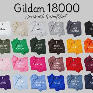 May include: A Gildan 18000 crewneck sweatshirt colour chart featuring twenty-four folded garments in various shades including white, sand, ash, sport grey, dark heather, black, military green, irish green, forest green, dark chocolate, gold, orange, light pink, safety pink, heliconia, heather sport maroon, red, maroon, purple, light blue, carolina blue, royal, indigo blue, and navy.