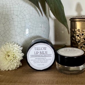 Unscented tallow lip balm in a glass jar beside a white flower and ceramic vase — natural handcrafted lip moisturizer made with organic tallow, honey, and beeswax.