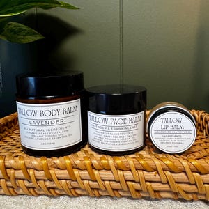 May include: Three dark amber glass jars with black lids containing skincare products. The labels read Tallow Body Balm Lavender 4oz, Tallow Face Balm Lavender & Frankincense 2oz, and Tallow Lip Balm Unscented 7ml, listing organic ingredients.