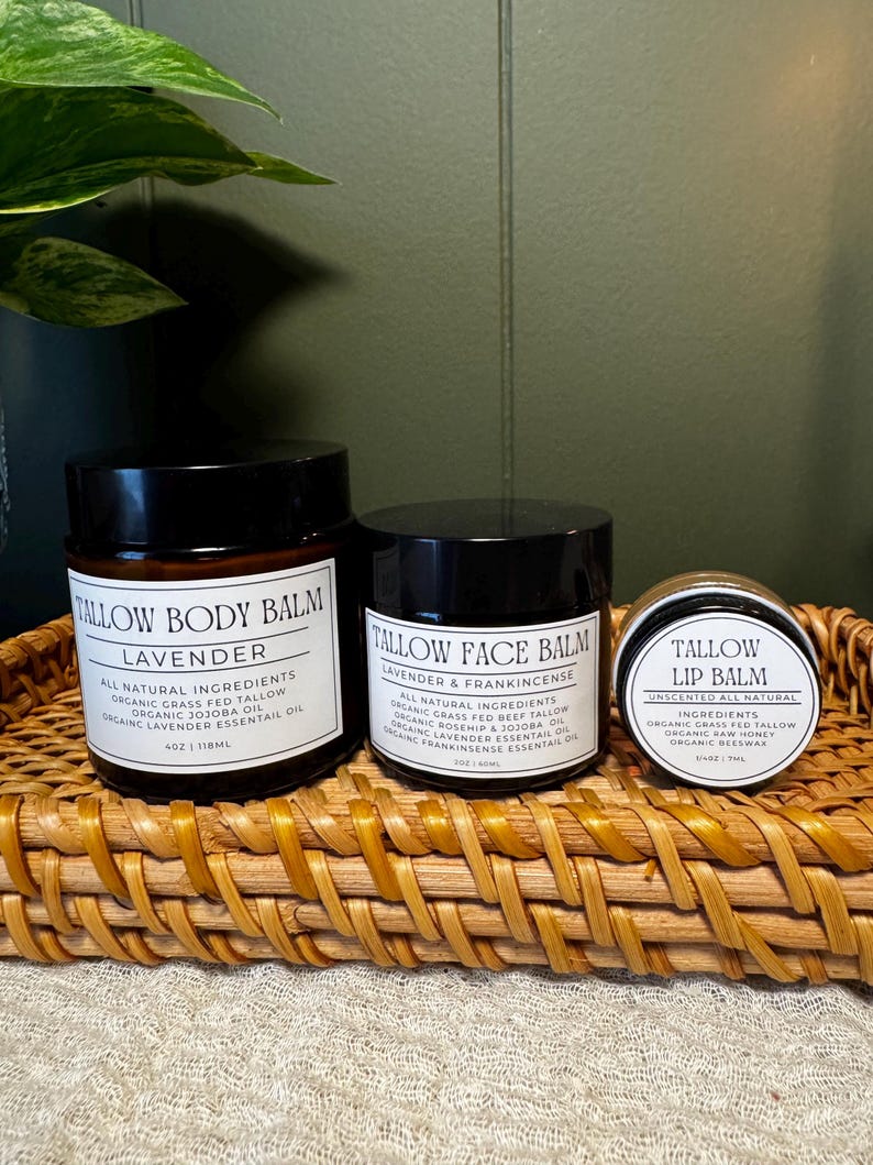 May include: Three dark amber glass jars with black lids containing skincare products. The labels read Tallow Body Balm Lavender 4oz, Tallow Face Balm Lavender & Frankincense 2oz, and Tallow Lip Balm Unscented 7ml, listing organic ingredients.