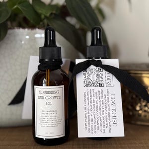 May include: Two amber glass bottles of hair growth oil with black droppers and labels. The labels read "Nourishing Hair Growth Oil" and list natural ingredients. Each bottle has a tag with instructions and a QR code.