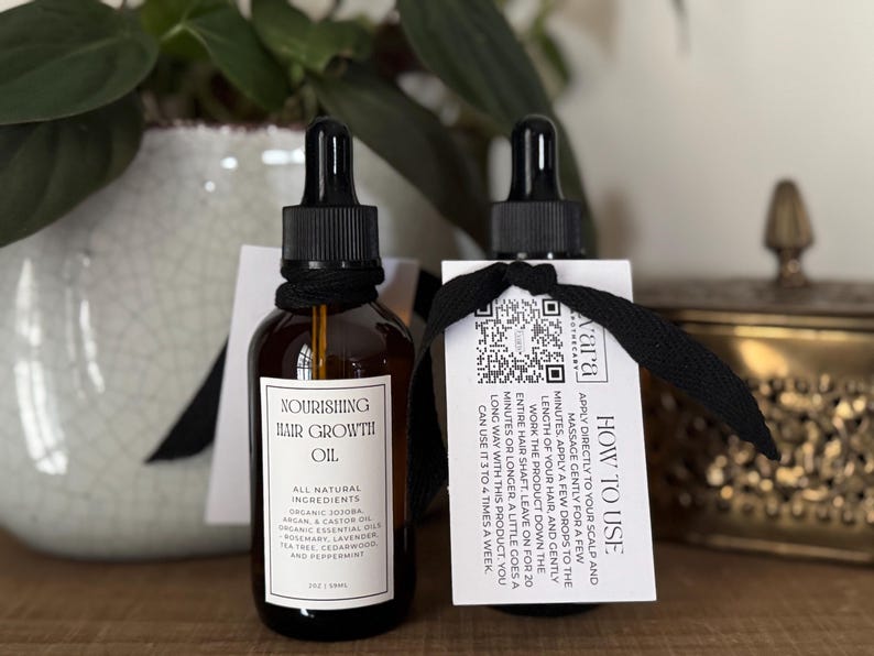 May include: Two amber glass bottles of hair growth oil with black droppers and labels. The labels read "Nourishing Hair Growth Oil" and list natural ingredients. Each bottle has a tag with instructions and a QR code.