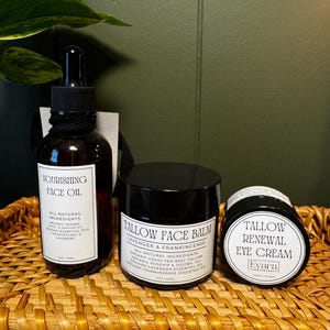 May include: A brown glass dropper bottle labeled Nourishing Face Oil, a black jar labeled Tallow Face Balm Lavender & Frankincense, and a smaller black jar labeled Tallow Renewal Eye Cream by Evara Apothecary, all containing 2oz or 15ml.
