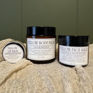 May include: Three amber glass jars with black lids containing skincare products. The small jar is Tallow Lip Balm 0.25 oz, the large center jar is Tallow Body Balm 4 oz, and the right jar is Tallow Face Balm 2 oz, all with white labels.