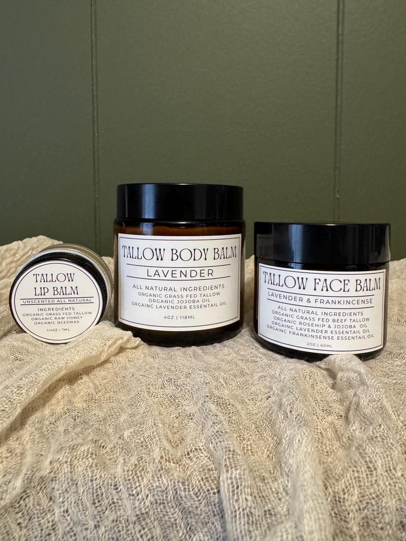 May include: Three amber glass jars with black lids containing skincare products. The small jar is Tallow Lip Balm 0.25 oz, the large center jar is Tallow Body Balm 4 oz, and the right jar is Tallow Face Balm 2 oz, all with white labels.