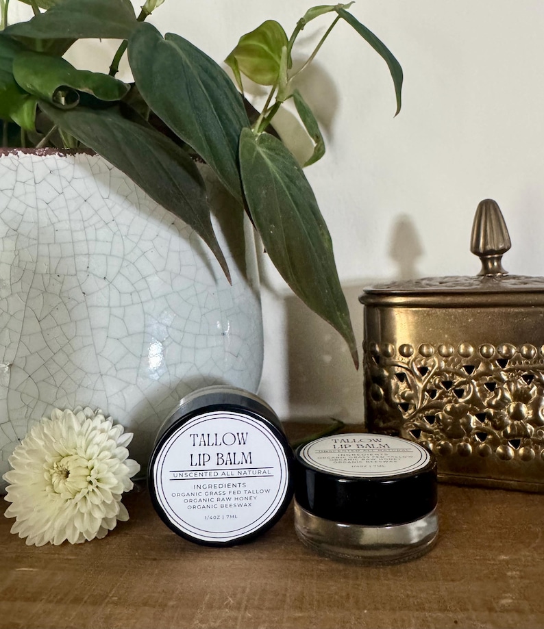 Unscented tallow lip balm in a glass jar beside a white flower and ceramic vase — natural handcrafted lip moisturizer made with organic tallow, honey, and beeswax.