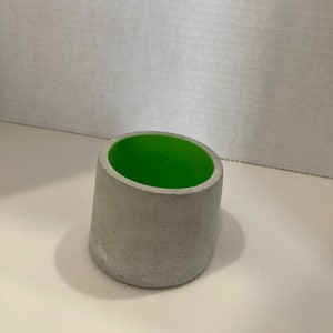 May include: A small, gray concrete planter with a bright green interior. The planter is round and has a slightly flared lip.