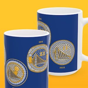 May include: Two blue and gold ceramic mugs with images of the Golden State Warriors championship trophies from 2018 and 2022. The mugs feature the Golden Gate Bridge and the year of the championship.