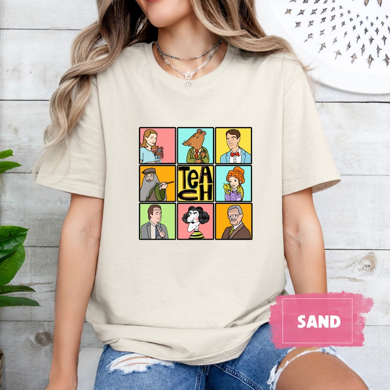 May include: Sand-colored t-shirt featuring a grid of cartoon characters in colorful squares. The word "TEACH" is in the center. The shirt is a neutral color, suitable for various outfits. The design is playful and eye-catching.