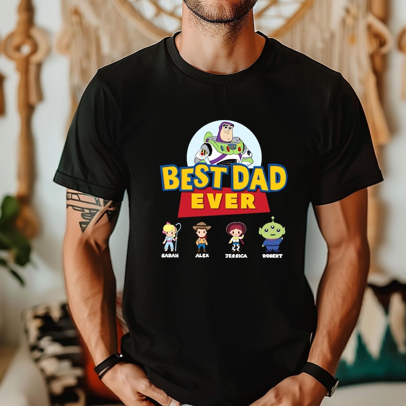 May include: Black t-shirt with the text "BEST DAD EVER" in yellow and blue, featuring cartoon characters. Below the text are four cartoon characters with names: Sarah, Alex, Jessica, and Robert.
