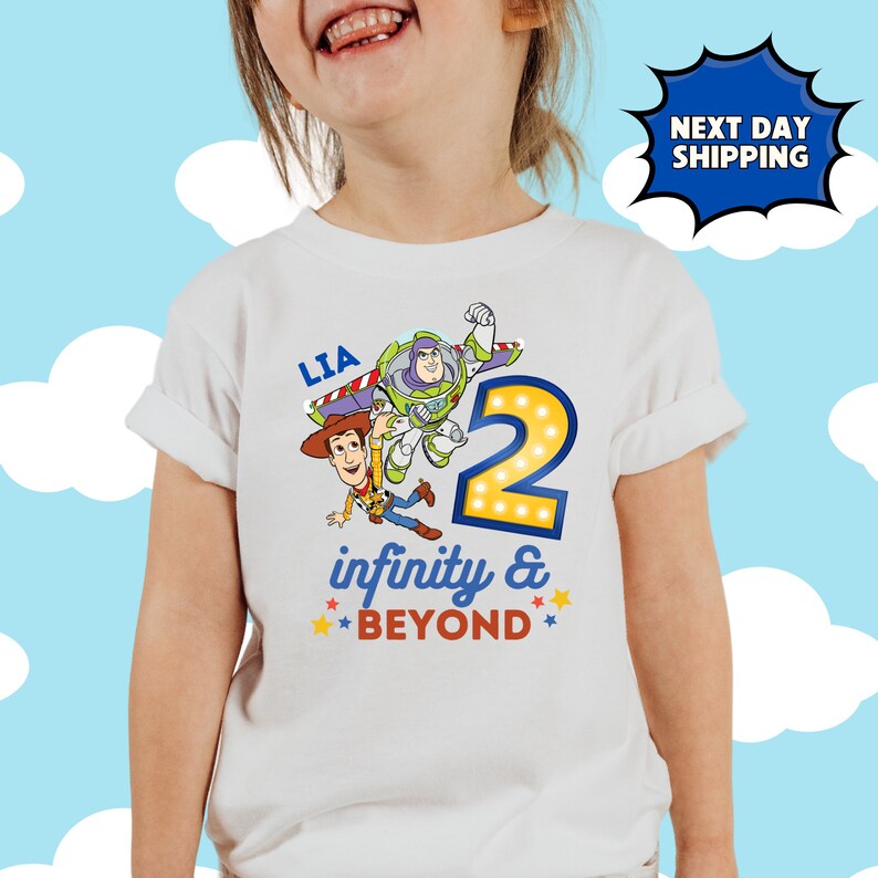 May include: White t-shirt with a blue and yellow number 2, a cartoon image of Buzz Lightyear and Woody from Toy Story, and the text "LIA infinity & BEYOND".