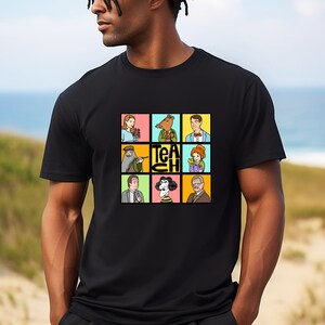 May include: Black t-shirt featuring a colorful graphic of nine cartoon characters in squares, with the word "TEACH" in the center. The characters include a woman with flowers, a bear, a man in a suit, and others.