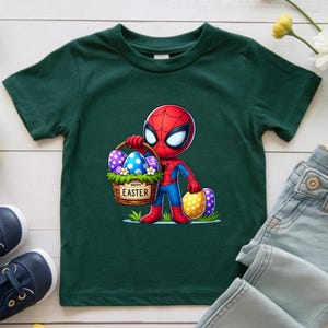 Puede incluir: Camiseta verde oscuro con un personaje de dibujos animados de Spider-Man sosteniendo una cesta de Pascua. La cesta tiene las palabras "HAPPY EASTER". El personaje lleva un traje rojo y azul. La camiseta es para ni&ntilde;os.
